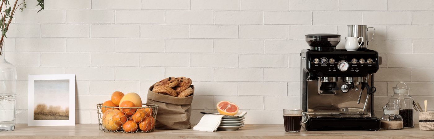 White skinny metro brick wall tiles from the Kennet collection in a kitchen behind a coffee machine, fruit bowl and bag of pastries.