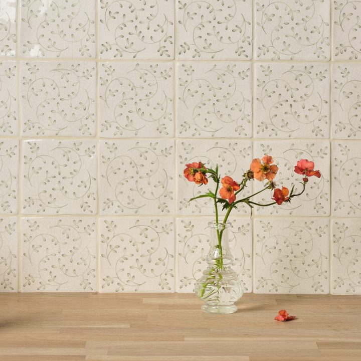 Wall of Sage Green leaf Pattern square tiles with jasmine grout behind an oak worktop and vase of orange flowers